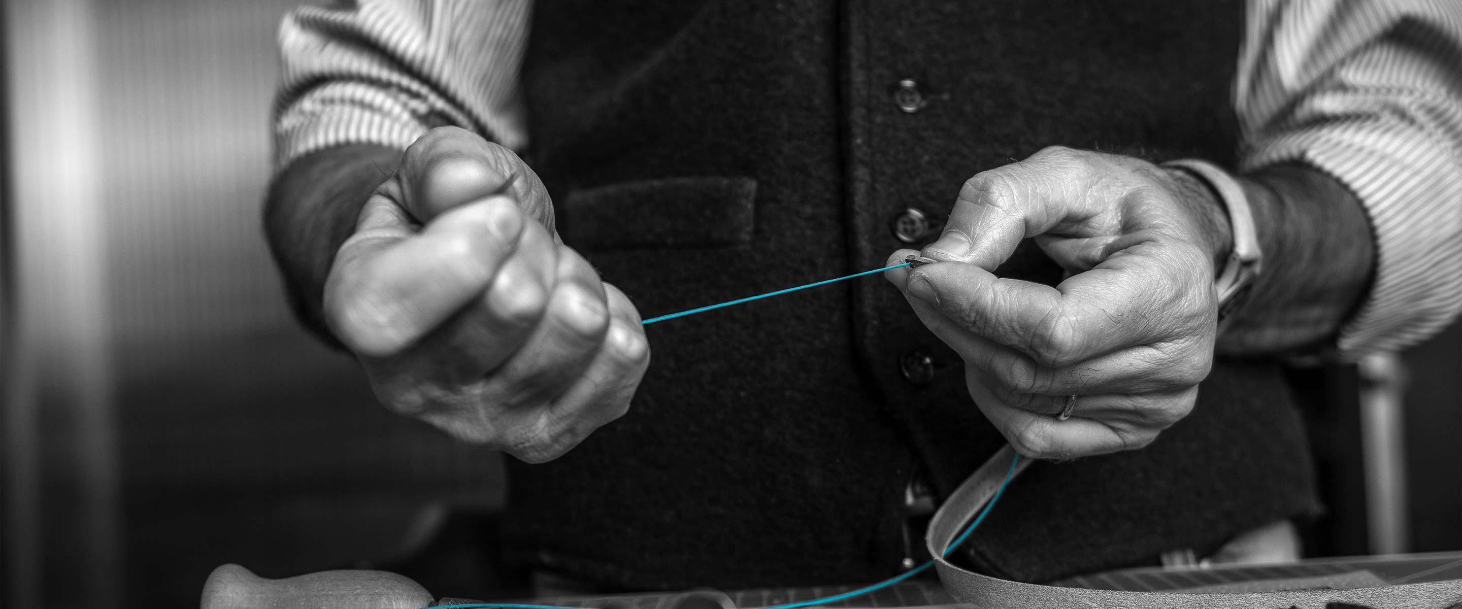 Schwarz-weiße Nahaufnahme der Hände eines Schneiders, der petrolfarbenen Faden misst